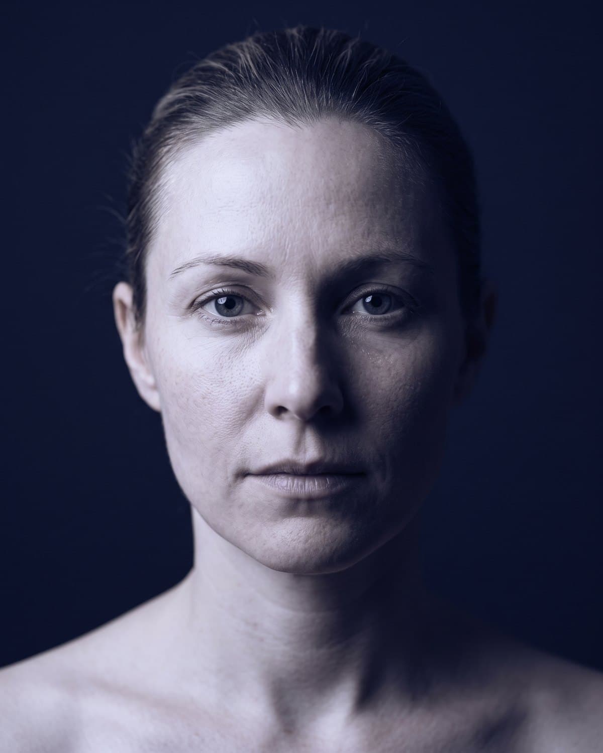 A woman's face lit from one side by a single cool light, the other side in shadow